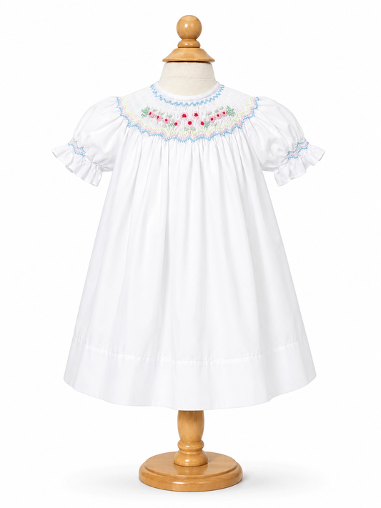 A white baby smocked dress with short ruffled sleeves and a floral embroidered yoke.