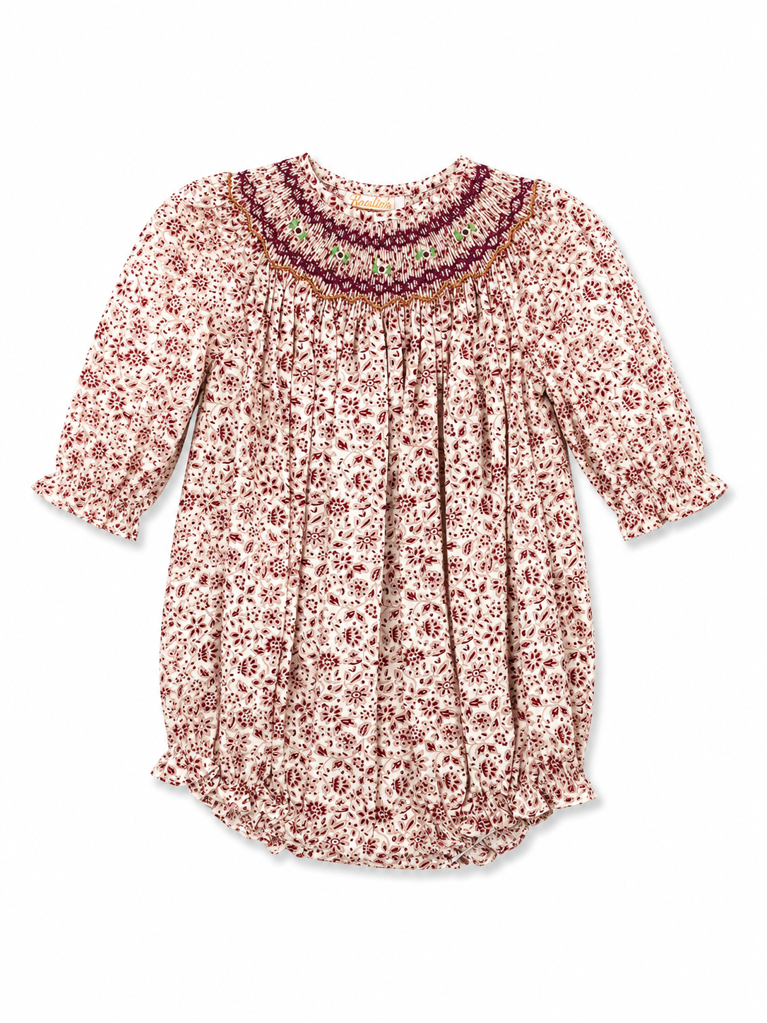 A long-sleeve babydoll-style top with a dense small floral print in dark red and brown on a warm cream background, featuring a smocked bodice and a decorative embroidered yoke.