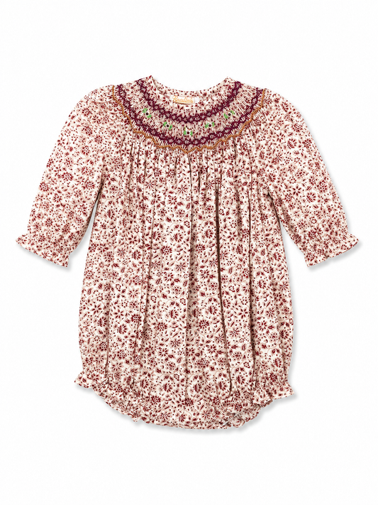A long-sleeve babydoll-style top with a dense small floral print in dark red and brown on a warm cream background, featuring a smocked bodice and a decorative embroidered yoke.